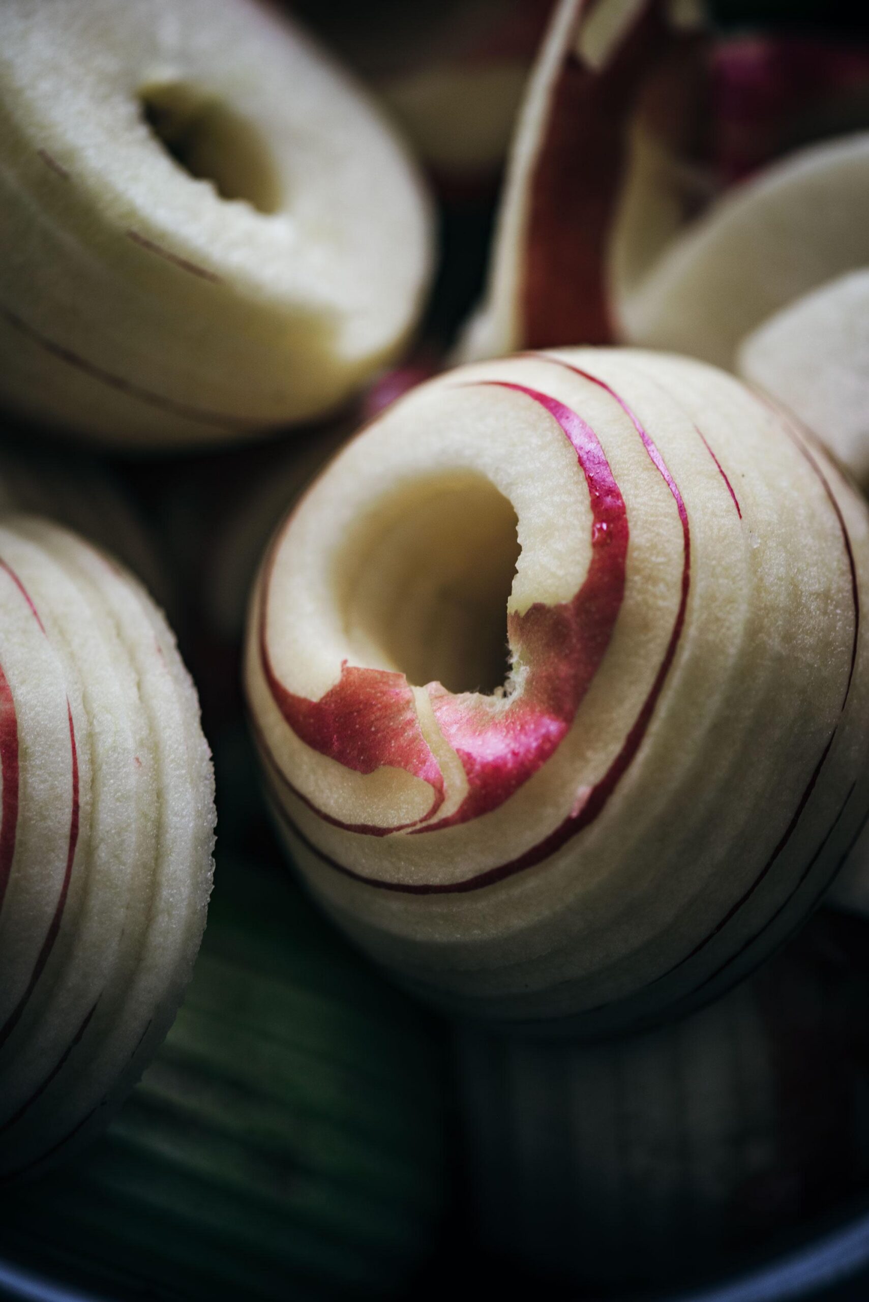 Close-up of peeled apples with some red skin left in spiral patterns, showing the texture and circular grooves made by a peeler—perfect for making smooth, flavorful apple butter.