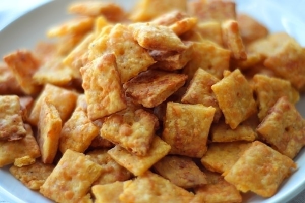 A plate piled with square, golden-brown cheese crackers, boasting a crisp texture and slightly uneven edges, showcases the irresistible appeal of classic cheese crackers.