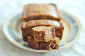 A loaf of Earl Grey Tea Loaf sits on a decorative plate, with several slices cut and one slice pulled forward, revealing its moist, textured interior and hint of aromatic tea flavor.