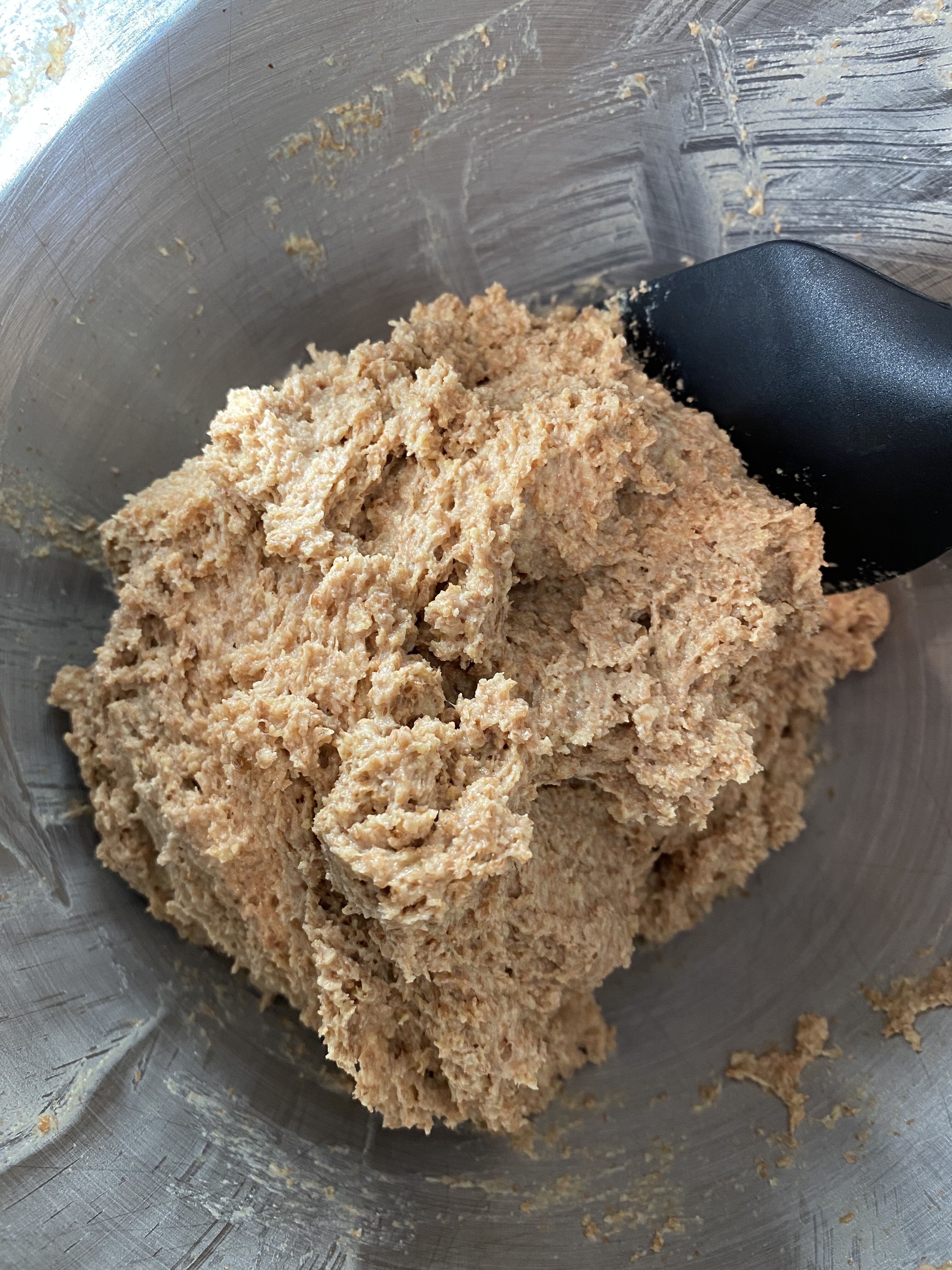 A close-up of a mound of coarse, brown dough for an Irish brown bread in a metal mixing bowl, with a black spatula partially visible on the right side—the perfect start to a no yeast bread recipe.