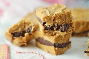 Close-up of Peanut Butter Fudge bars with a thick layer of chocolate in the center, stacked on parchment paper. The bars have a crumbly texture and appear rich and creamy.