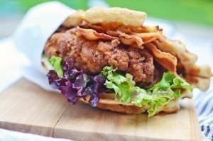 A close-up of a Crispy Chicken Waffle Wrap with crispy bacon, fresh lettuce, and a soft bun, placed on a wooden board.