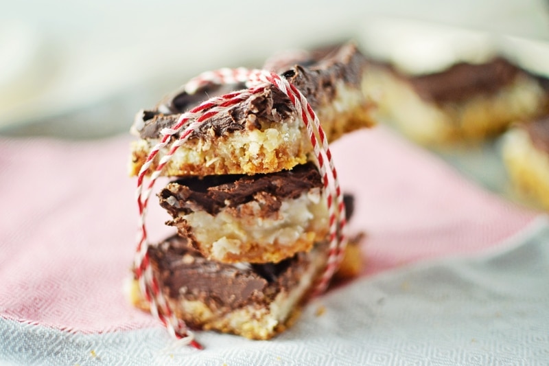 Three chocolate-covered cookie bars are stacked and tied with red and white string, placed on a pink and white cloth.