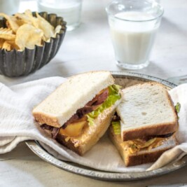 A black metal bowl with potato chip, glass of milk, and a sliced loaded BLT sandwich with Pepperidge Farm hearty white bread.