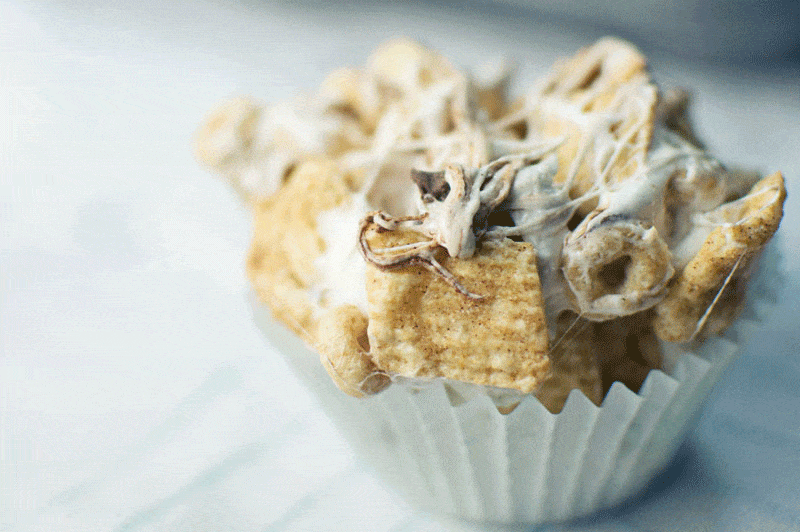 A close-up of Marshmallow Cupcakes in a white cupcake liner, made with square cereal pieces and Cheerios, all coated and held together by gooey melted marshmallow.
