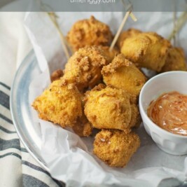 A plate of golden-brown hushpuppies sits on parchment paper with a small bowl of dipping sauce, served on a striped cloth. The image features the text Hushpuppies and LittleFiggy.com at the top.