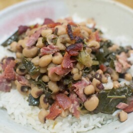 A bowl of white rice topped with savory Black Eyed Peas, collard greens, and pieces of ham, served with a fork on the side.