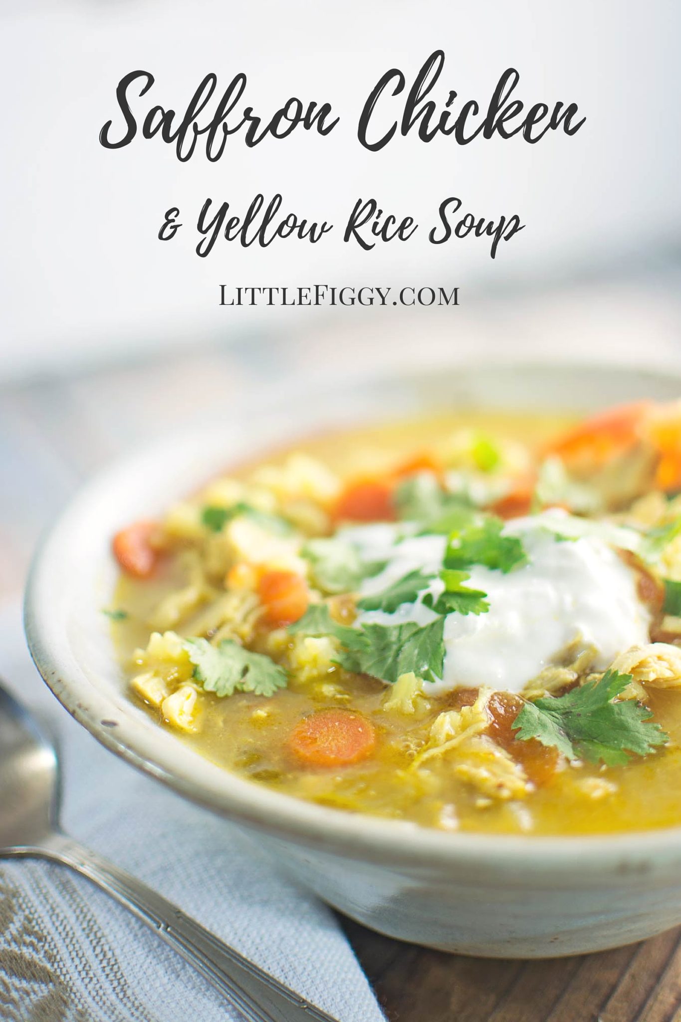A bowl of saffron chicken soup and yellow rice, topped with fresh cilantro and a dollop of sour cream, sits on a wooden table next to a spoon; text above reads Saffron Chicken & Yellow Rice Soup.