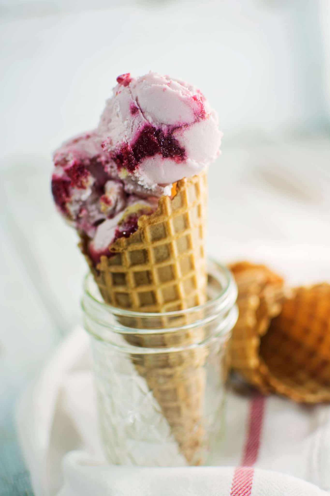 Two scoops of swirled Raspberry Cheesecake ice cream in a waffle cone. 