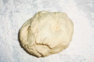 A ball of raw dough sits on a floured surface, ready to be kneaded and shaped into delicious homemade pretzels for baking.