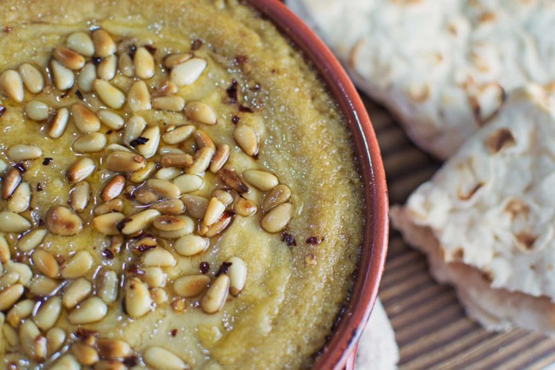 Try this Baked Hummus topped off with buttery, toasted pine nuts and served up with some pita bread! It's great for your next get together, or as a snack. Recipe @LittleFiggyFood