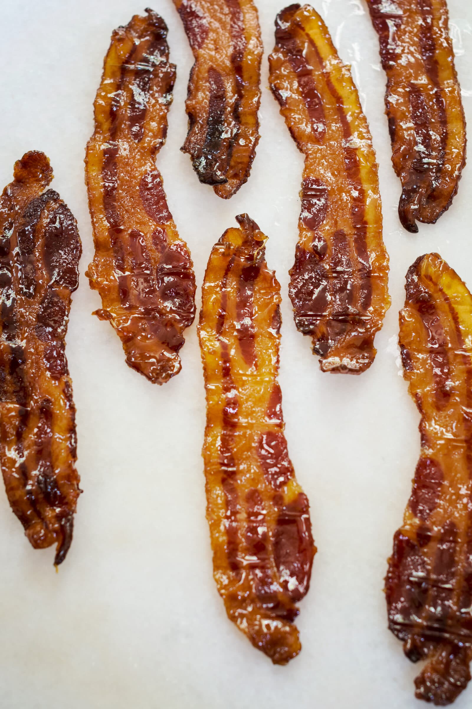 Eight strips of crispy, cooked bacon—reminiscent of irresistible Pig Candy—are laid out on a white surface, glistening slightly with grease.