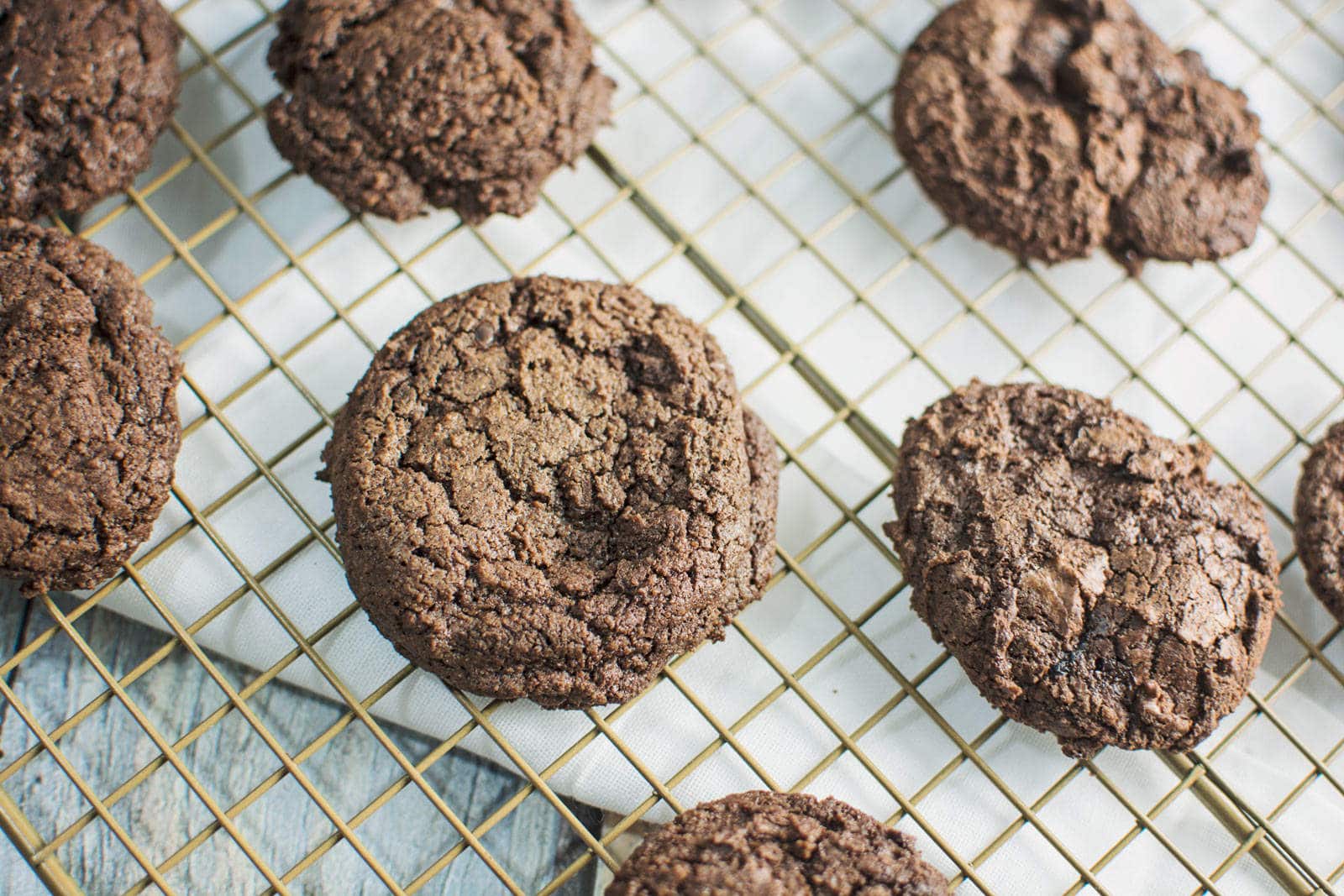 Several Mocha Cookies cooling on a wire rack over a white cloth. The cookies are round with a cracked surface and appear soft and chewy.