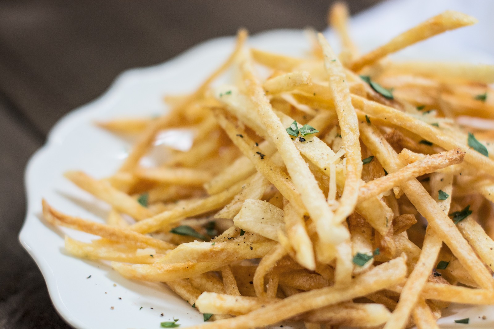 A close-up of a white plate filled with thin, crispy fries garnished with chopped herbs.
