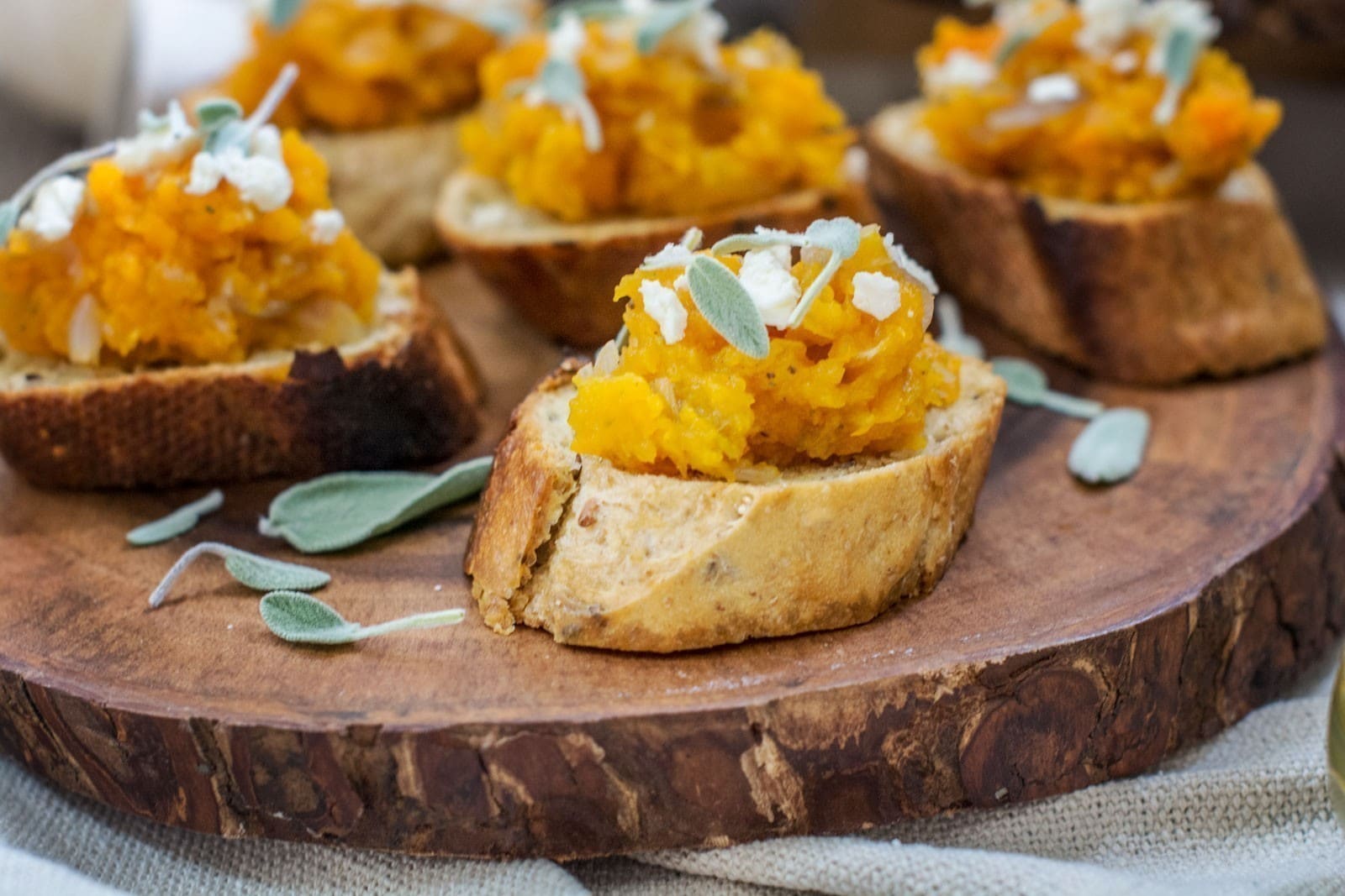 Slices of toasted bread topped with mashed squash, crumbled cheese, and fresh sage leaves make this Butternut Bruschetta a perfect rustic appetizer.