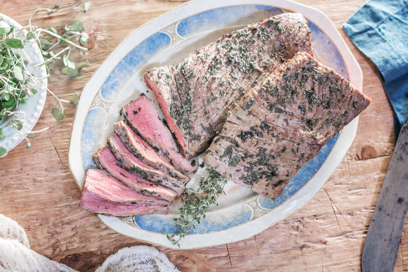 A Roast Beef platter with herb-crusted roast beef, partially sliced to show pink meat inside, garnished with fresh herbs, on a wooden table.