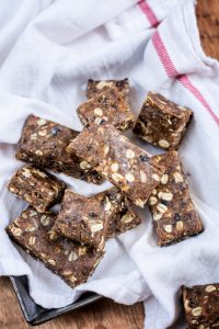 Homemade fig bars with visible oats and seeds are arranged on a white cloth with a red stripe, atop a wooden surface.