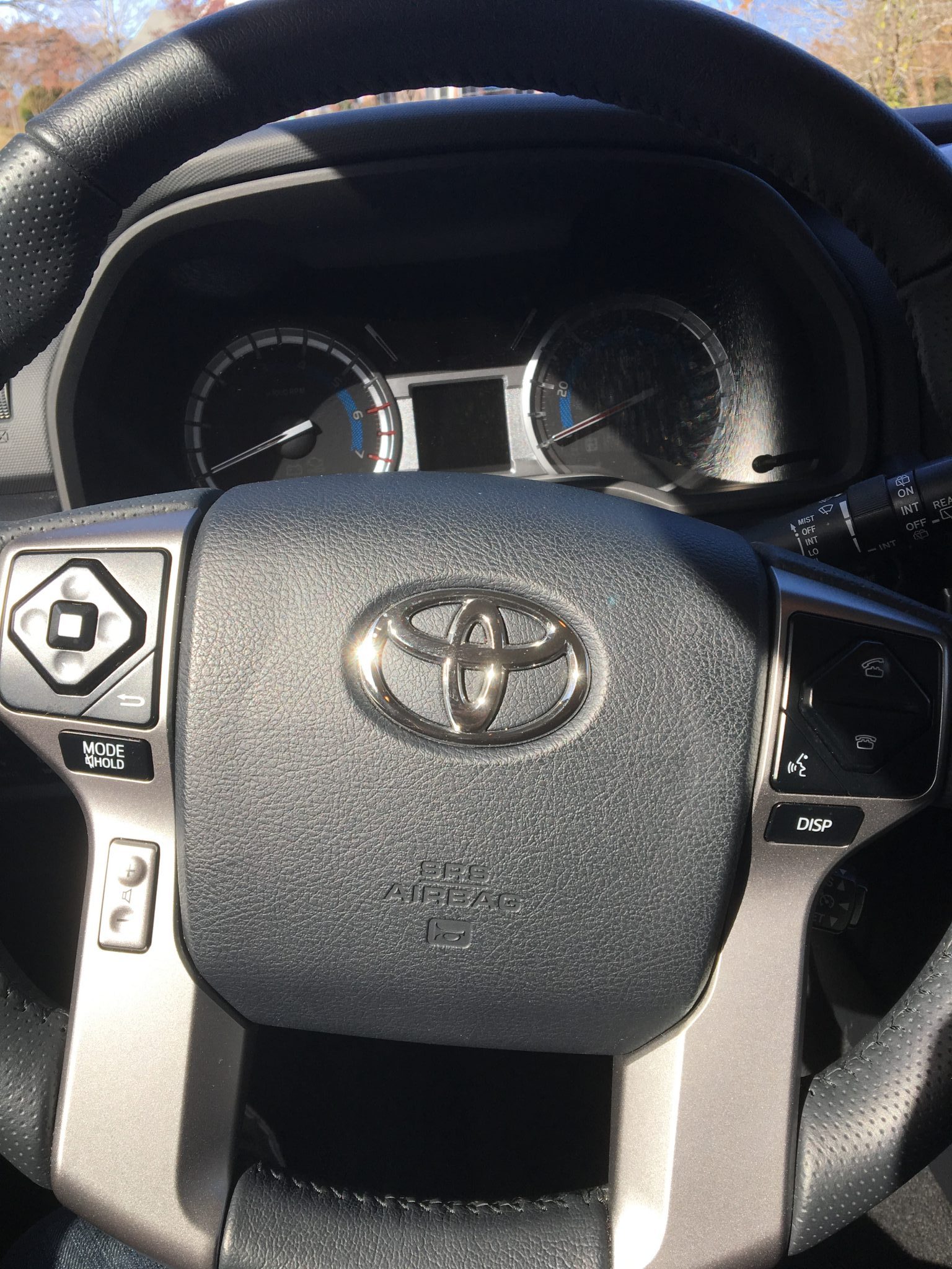 Close-up of a Toyota car steering wheel with control buttons on both sides, dashboard gauges in the background, and sunlight illuminating the interior—perfect for road trips with a pack of Fig Bars within reach.