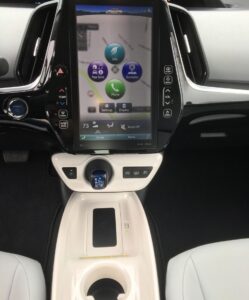 Center console of a modern car with a large touchscreen display showing navigation and app icons, gear selector, cup holders—perfect for your blondies—and climate control buttons. The interior features a sleek, black-and-white design.
