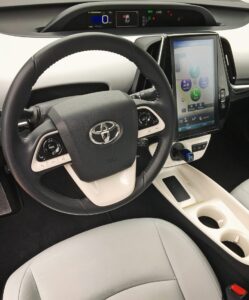 The image shows the interior of a Toyota car, focusing on the steering wheel, large touchscreen display, dashboard gauges, and center console with cup holders—perfect for keeping snacks like Blondies close while you drive.