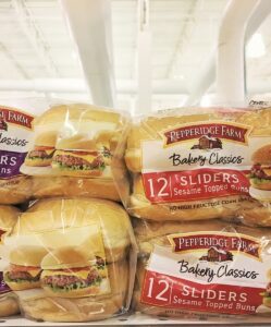 Bags of Pepperidge Farm Bakery Classics slider buns, like Sliders White Buns and Sliders Sesame Topped Buns, are displayed on a store shelf. Each bag highlights mouthwatering sliders and contains 12 soft buns.