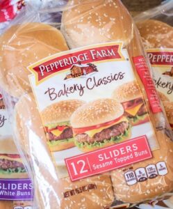Three bags of Pepperidge Farm Bakery Classics slider buns, perfect for sliders, including white and sesame topped varieties, are arranged on a wooden surface. Each bag contains 12 buns and features images of burgers on the packaging.