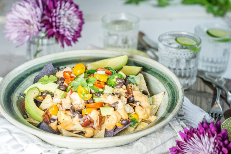 Lobster nachos topped with avocado slices in a green rimmed bow. 