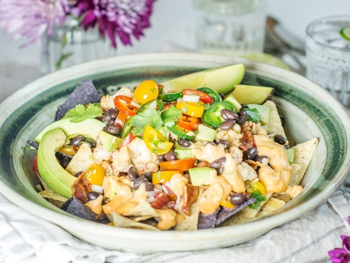 Plate of nachos with avocado and vegetables.