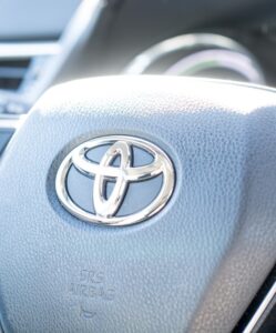 Close-up of a Toyota steering wheel, with the Toyota logo in the center, control buttons on both sides, and SRS AIRBAG text below the logo—perfect for your next road trip to enjoy Lobster Nachos. The dashboard is visible in the background.