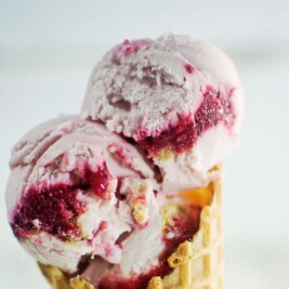 Raspberry ice cream in waffle cone on glass jar.