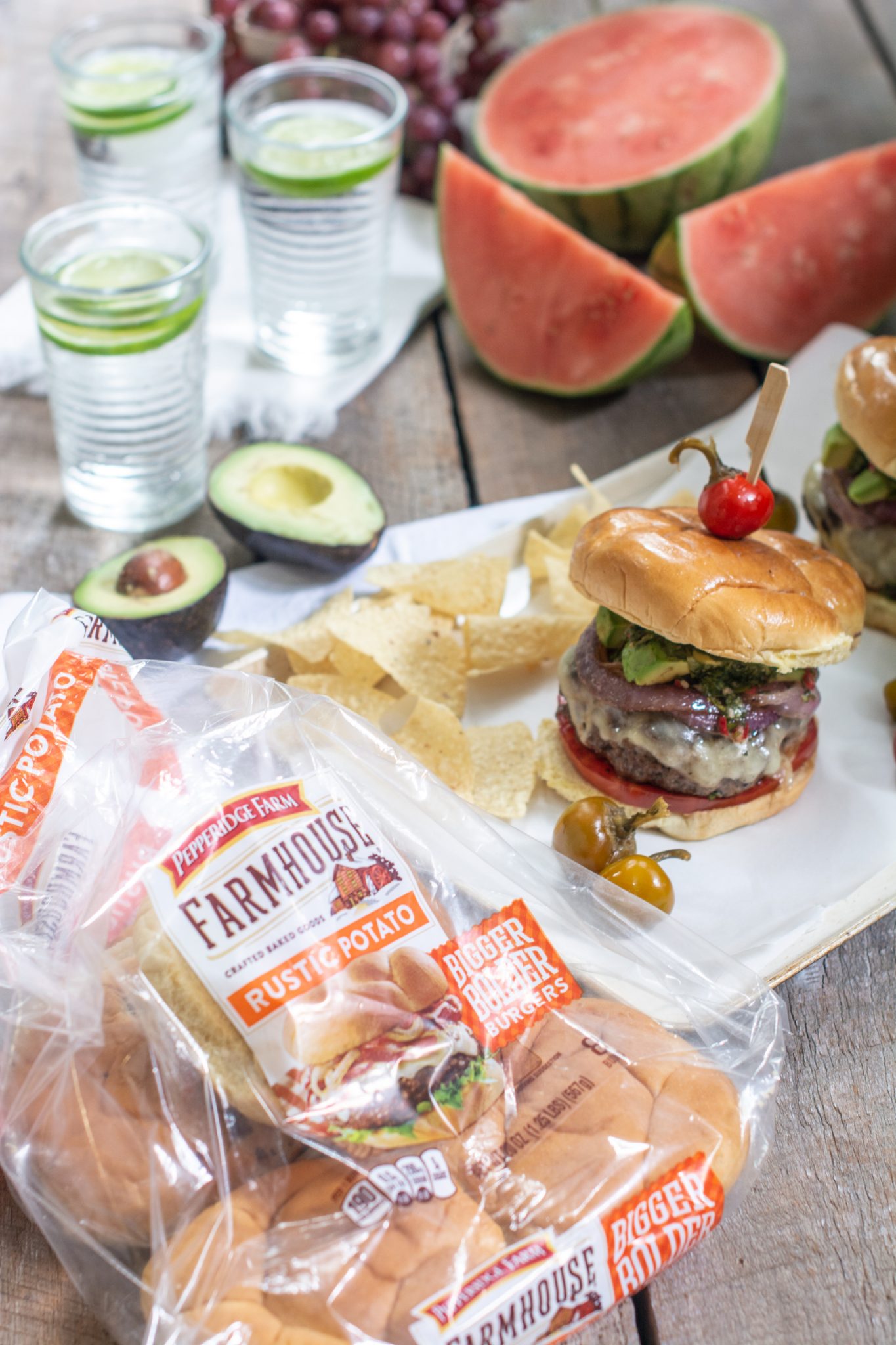 Chimichurri burgers on table with avocado halves and Pepperidge Farm Hamburger buns.