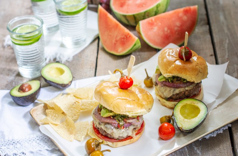 Tabletop with chimichurri burgers, fruit and glasses of water with lime.