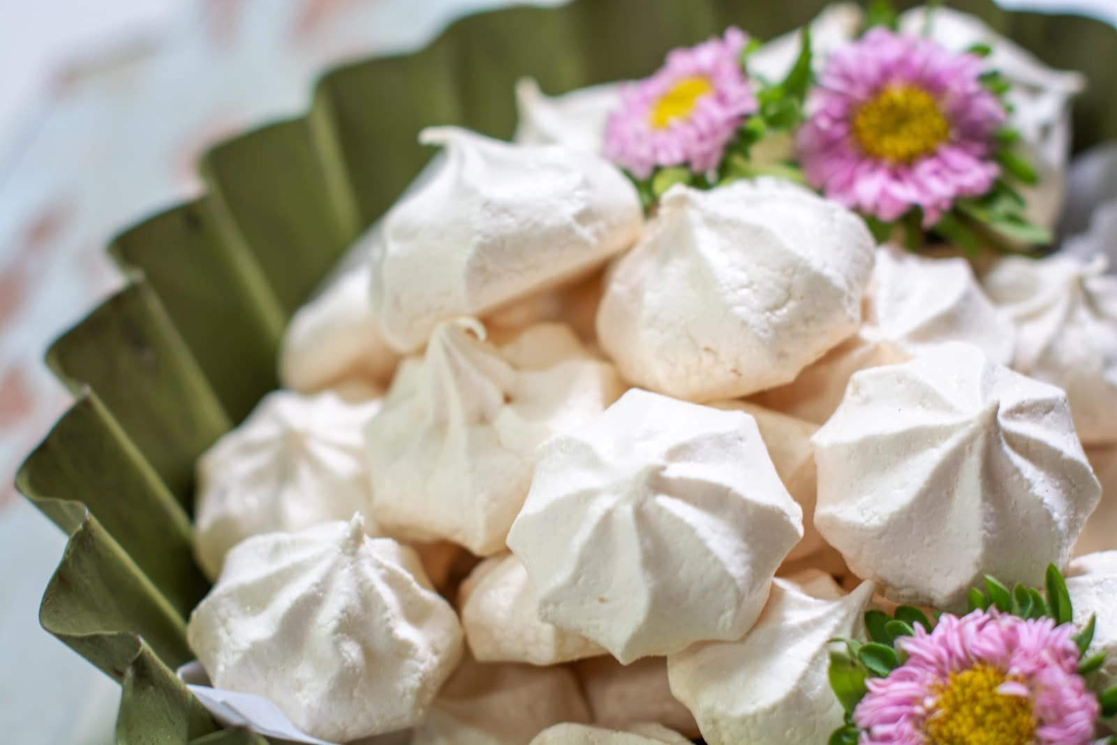 A close-up of easy meringue cookies arranged in a green dish, decorated with pink and yellow flowers.