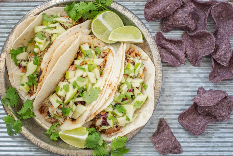 A plate of BBQ pulled pork tacos and a side of blue corn tortilla chips