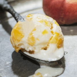 Spoonful of peach ice cream on metal tray.