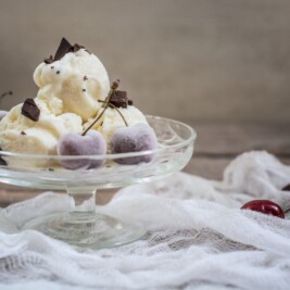 Scoops of homemade vanilla ice cream served with chocolate pieces and cherries