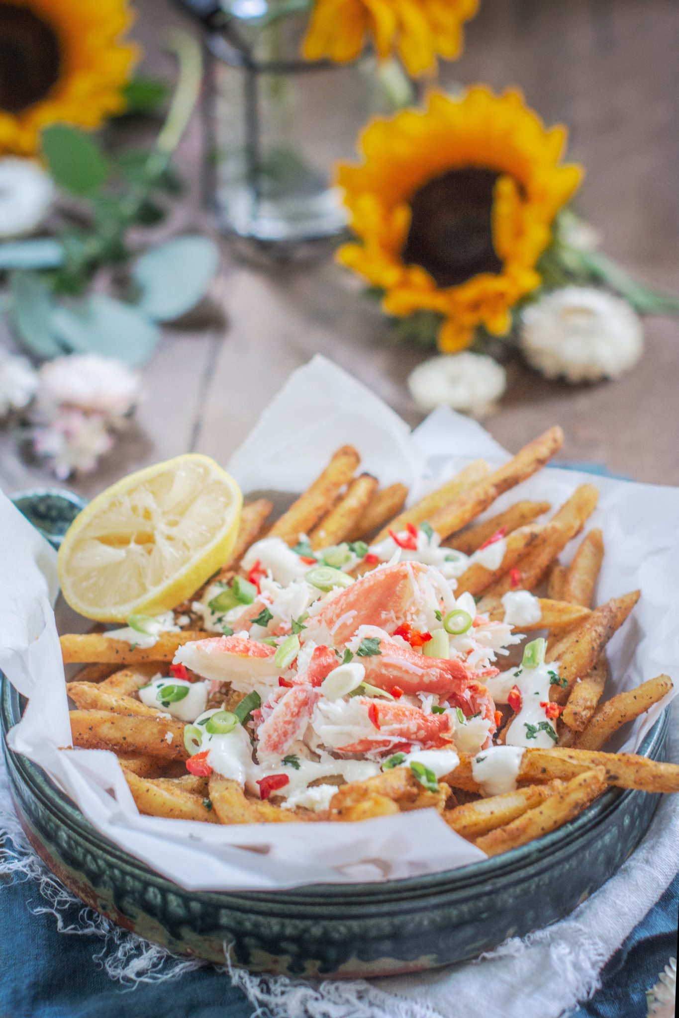 Loaded Crab Fries on brown table with sunflowers in the background