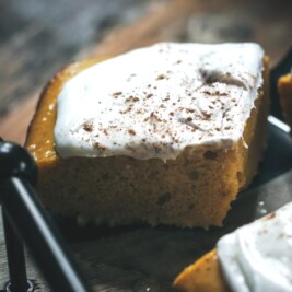 Pumpkin cake slice with creamy frosting on tray.