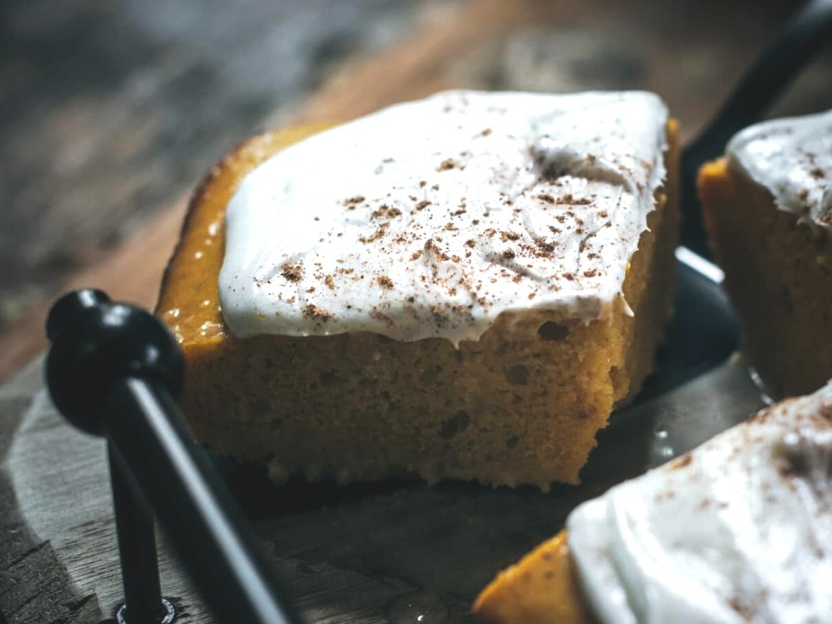 Pumpkin cake slice with creamy frosting on tray.