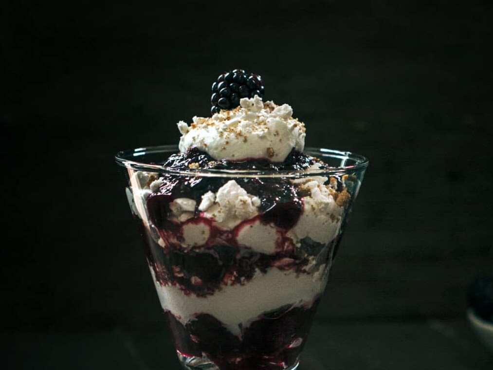 Blackberry parfait with whipped cream in glass.