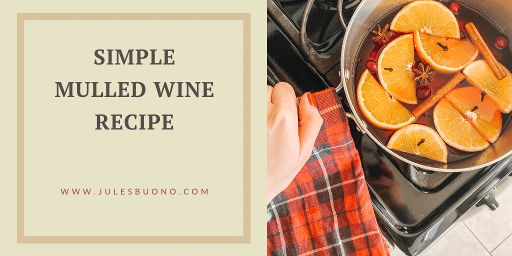 A hand holds a plaid towel near a stovetop pot filled with mulled wine, orange slices, cranberries, and cinnamon sticks. Text reads: “Simple Mulled Wine Recipe. www.julesbuono.com.”.