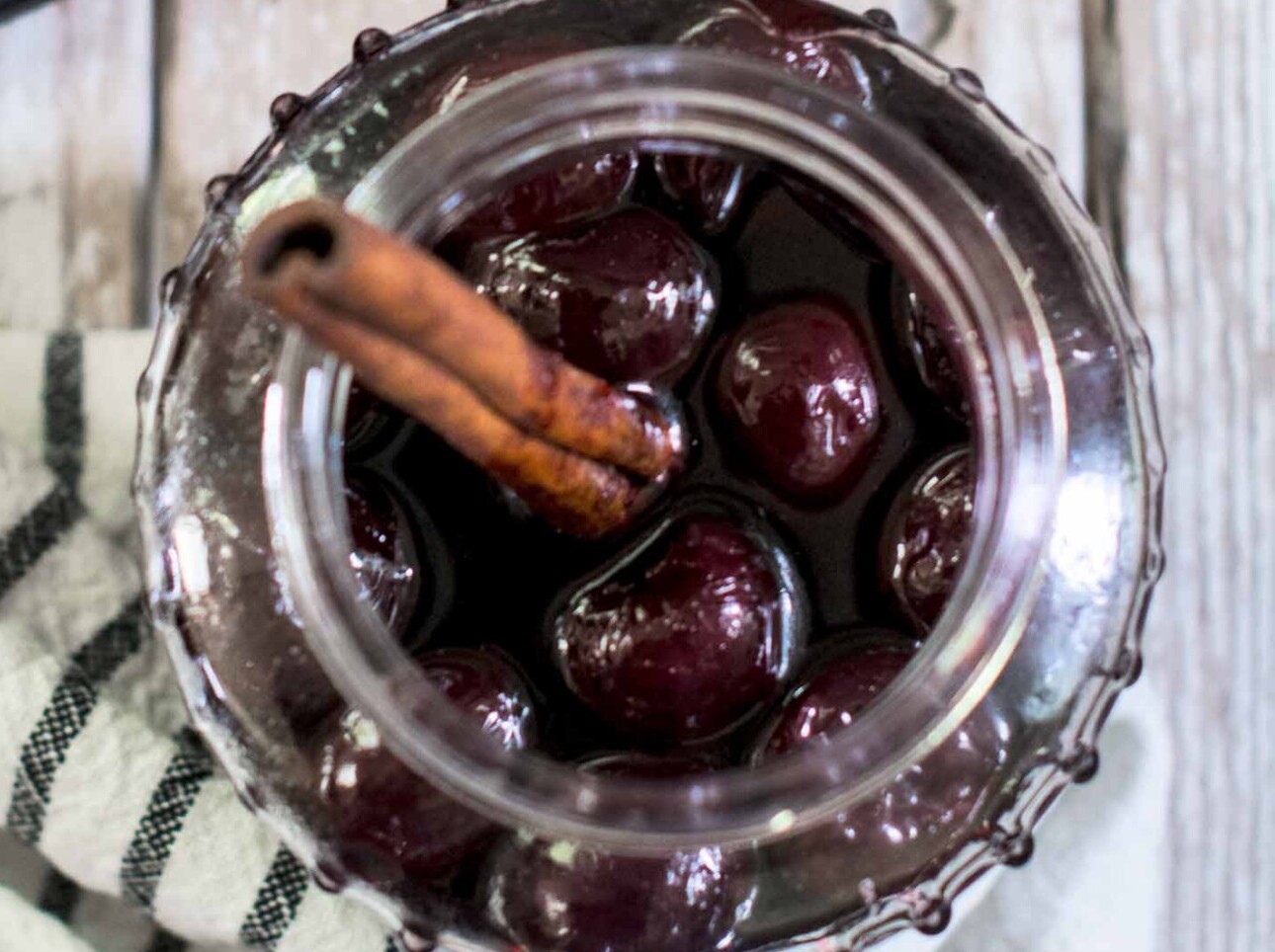 Homemade pickled cherries in a glass jar with cinnamon.