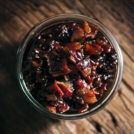 Jar of savory bacon jam on wooden table.