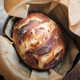 Crusty loaf of bread in parchment-lined pot.