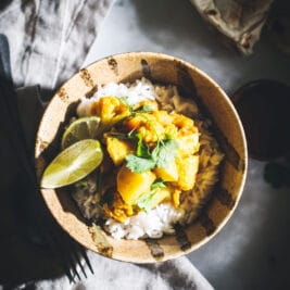 Vegetable curry in bowl with rice and cilantro on white table and napkin