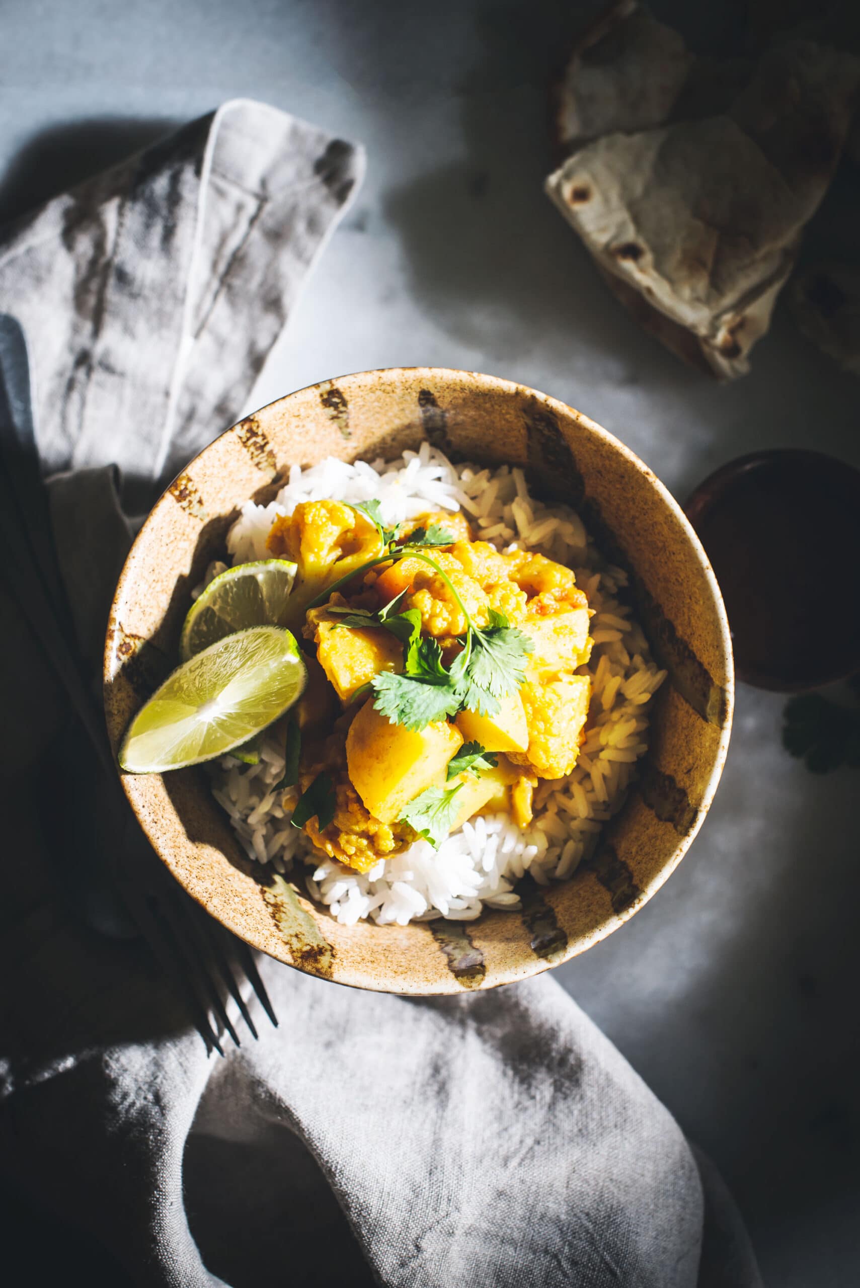 Vegetable curry in bowl with rice and cilantro on white table and napkin