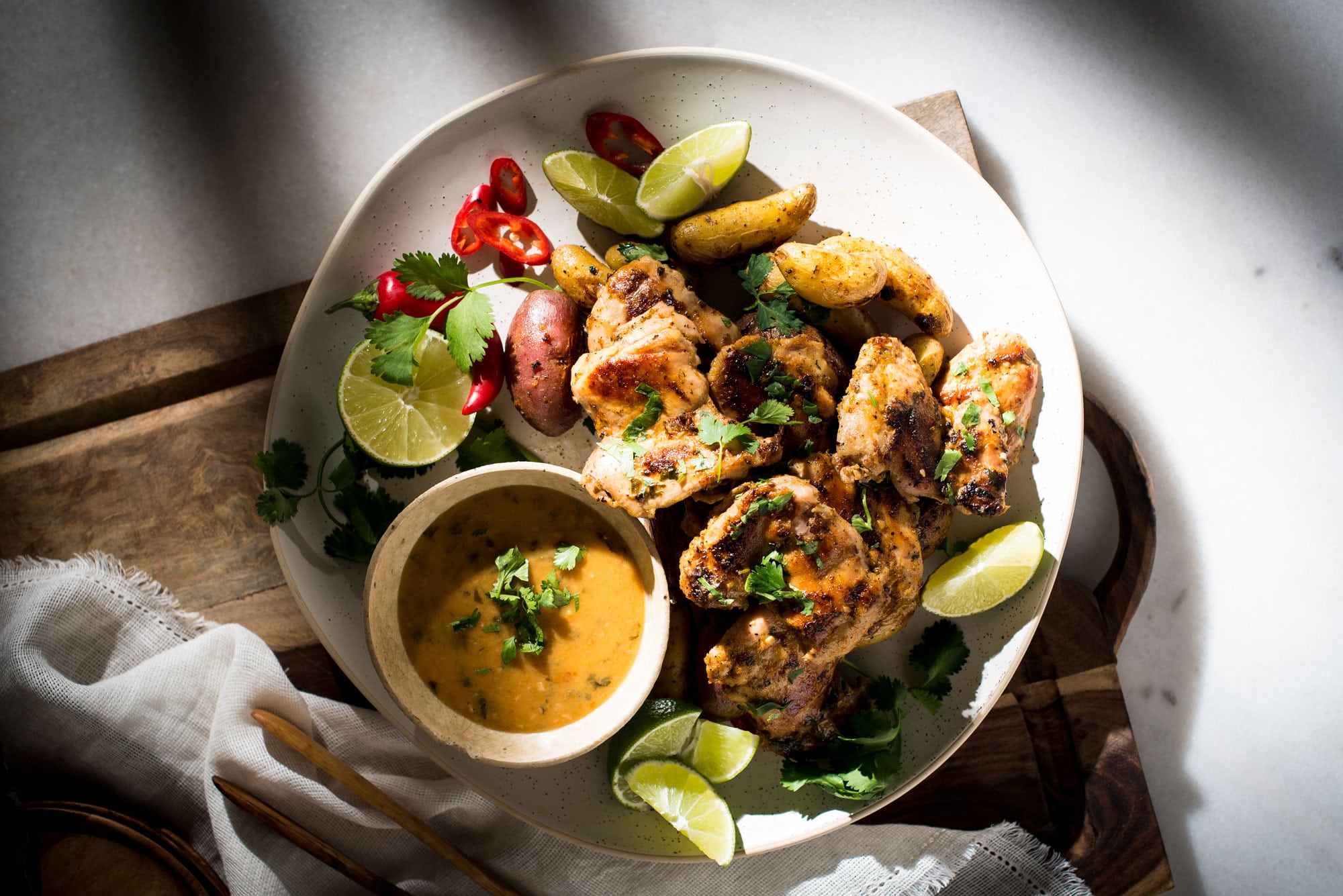 White platter with chicken thighs and bowl of spicy sauce