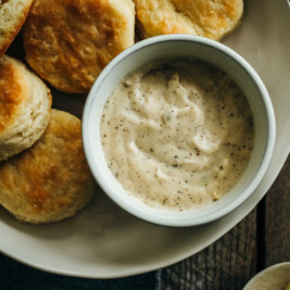 Close-up overhead view of flaky biscuits on a plate beside a bowl of creamy peppered gravy.