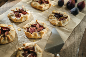 Golden fig galettes cooling on parchment paper with honey drizzles and fresh figs nearby, creating a cozy homemade dessert scene