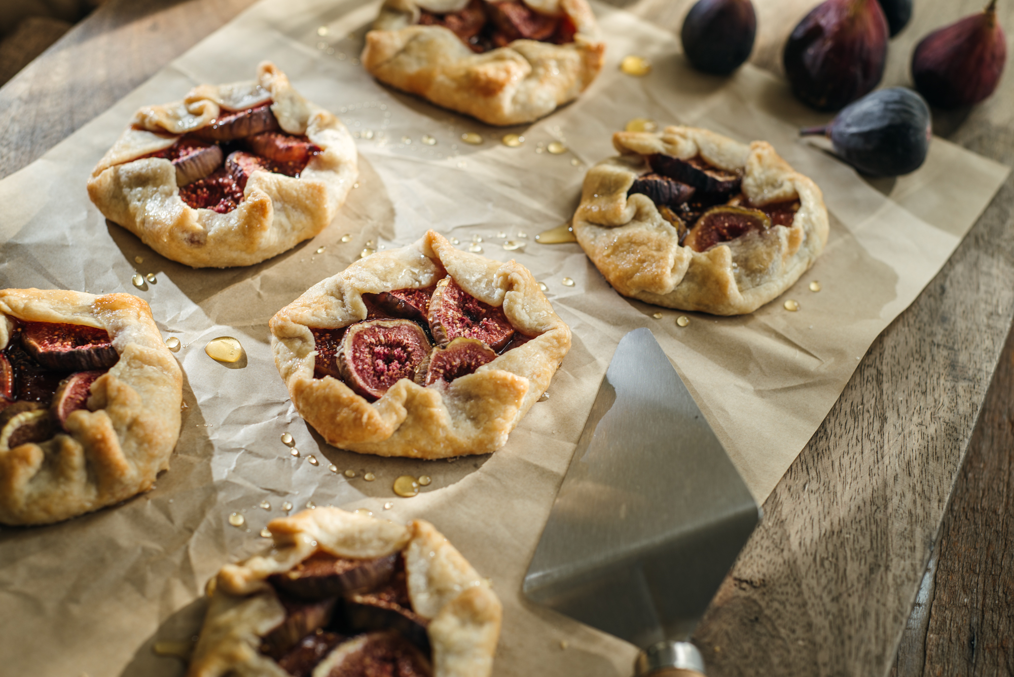 Golden fig galettes cooling on parchment paper with honey drizzles and fresh figs nearby, creating a cozy homemade dessert scene